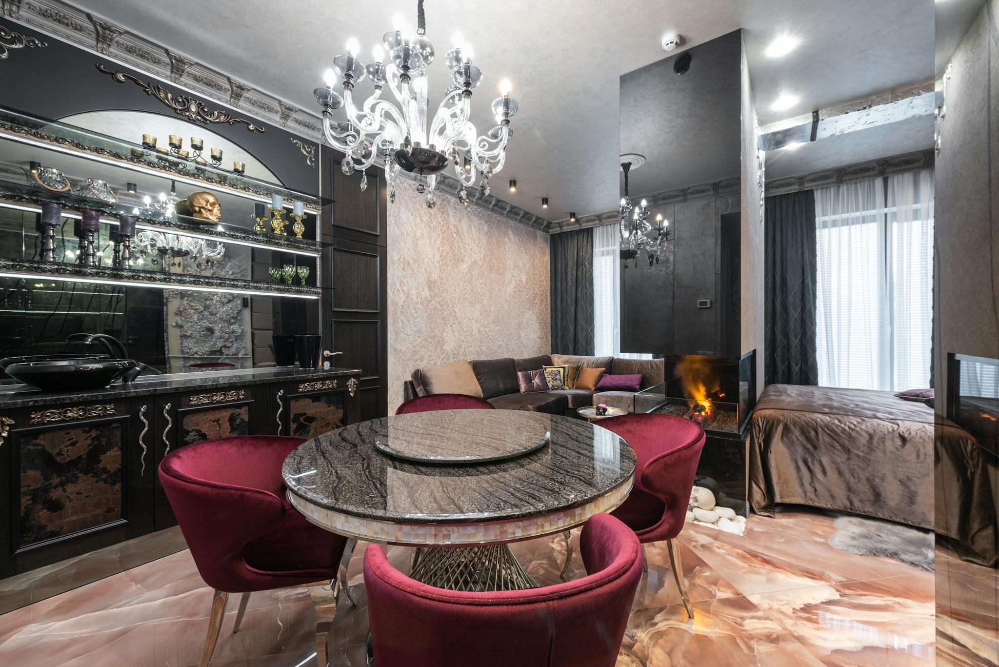 Armchairs at table placed near kitchen counter with kitchenware in modern spacious apartment with bed near burning fireplace and couch
